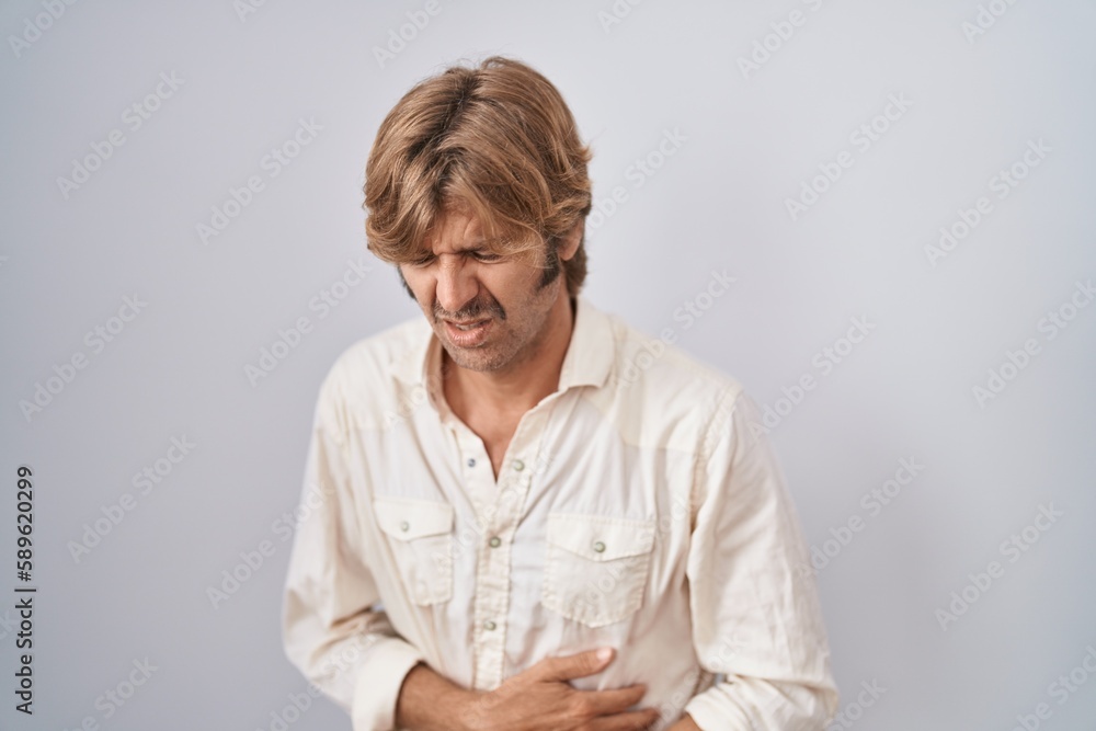 Wall mural Middle age man standing over isolated background with hand on stomach because indigestion, painful illness feeling unwell. ache concept.