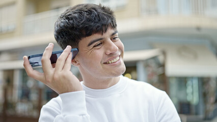 Young hispanic man listening to voice message at coffee shop terrace