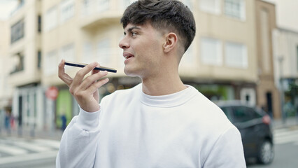 Young hispanic man sending voice message with smartphone at street