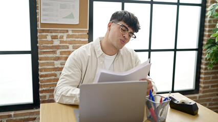 Young hispanic man business worker using laptop reading document at office