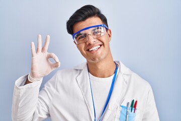 Hispanic man working as scientist smiling positive doing ok sign with hand and fingers. successful expression.
