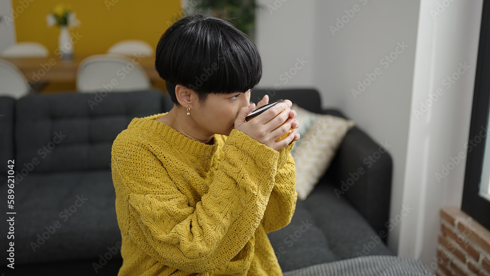 Poster young chinese woman drinking coffee sitting on sofa at home