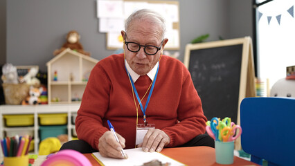 senior working as teacher writing on papers and talking at kindergarten