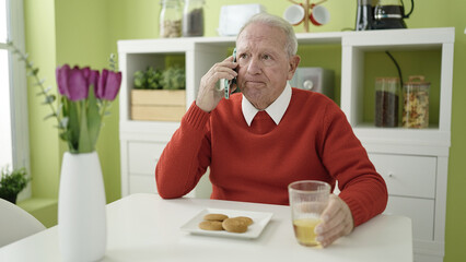 senior eating cookies and drinking juice speaking on the phone at home
