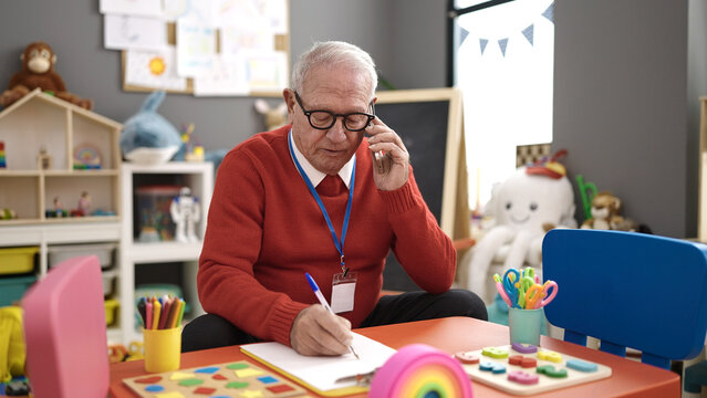 senior working as teacher writing on clipboard speaking on the telephone at kindergarten