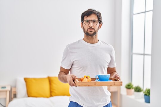 Handsome latin man eating breakfast on the bed relaxed with serious expression on face. simple and natural looking at the camera.