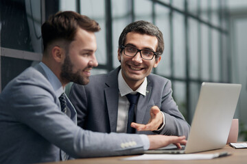 Obraz premium Two young businessmen sitting at workplace and working together in office