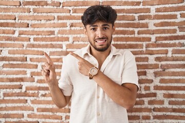 Arab man with beard standing over bricks wall background pointing aside worried and nervous with both hands, concerned and surprised expression