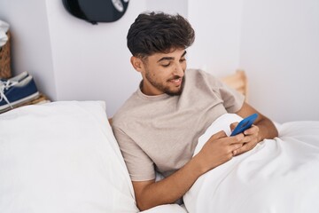 Obraz premium Young arab man using smartphone sitting on bed at bedroom