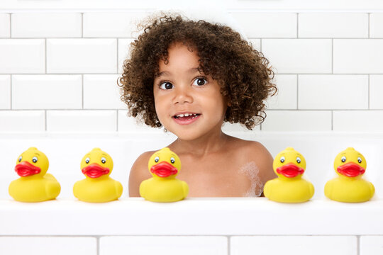 Smiling young girl with afro hair playing in bathtub with rubber ducks