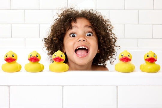 Naklejki Funny young girl with afro hair playing in bathtub with rubber ducks making funny face