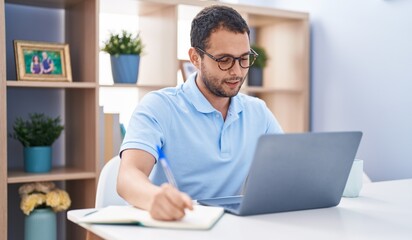 Young man using laptop writing on notebook at home
