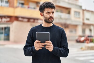 Young arab man with relaxed expression using touchpad at street