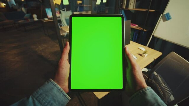 Close up hands man holding scrolling a vertical tablet computer with a green screen in the office. Mock-up display. Device. Apartment