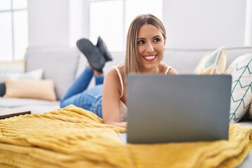 Young beautiful hispanic woman using laptop lying on table at home