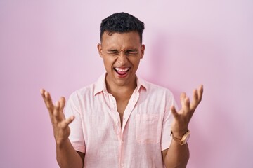 Young hispanic man standing over pink background celebrating mad and crazy for success with arms...