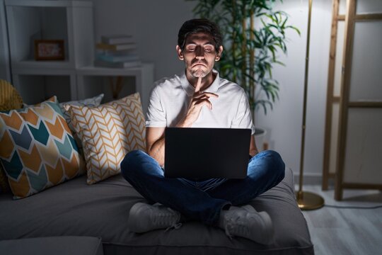 Young hispanic man using laptop at home at night thinking concentrated about doubt with finger on chin and looking up wondering