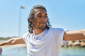 Young hispanic man doing yoga exercise standing at beach