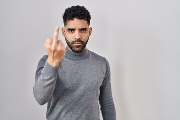 Hispanic man with beard standing over white background showing middle finger, impolite and rude fuck off expression