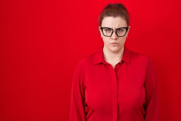 Young hispanic woman with red hair standing over red background skeptic and nervous, frowning upset because of problem. negative person.