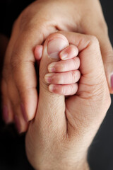 Close up little hand of child and palm of mother and father. The newborn baby has a firm grip on the parent's finger after birth. Parenting, childcare and healthcare concept. Professional macro photo - obrazy, fototapety, plakaty