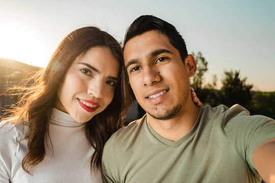 Pareja tom&aacute;ndose una foto en el atardecer con el sol detr&aacute;s de ellos