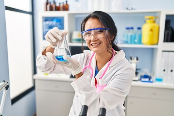 Young chinese woman wearing scientist uniform holding test tube at laboratory