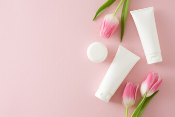 Organic skincare concept. Top view photo of cosmetic tubes without label cream jar and pink tulips on isolated pastel pink background with copy space