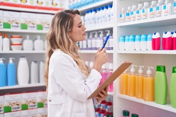Young blonde woman pharmacist writing on document at pharmacy