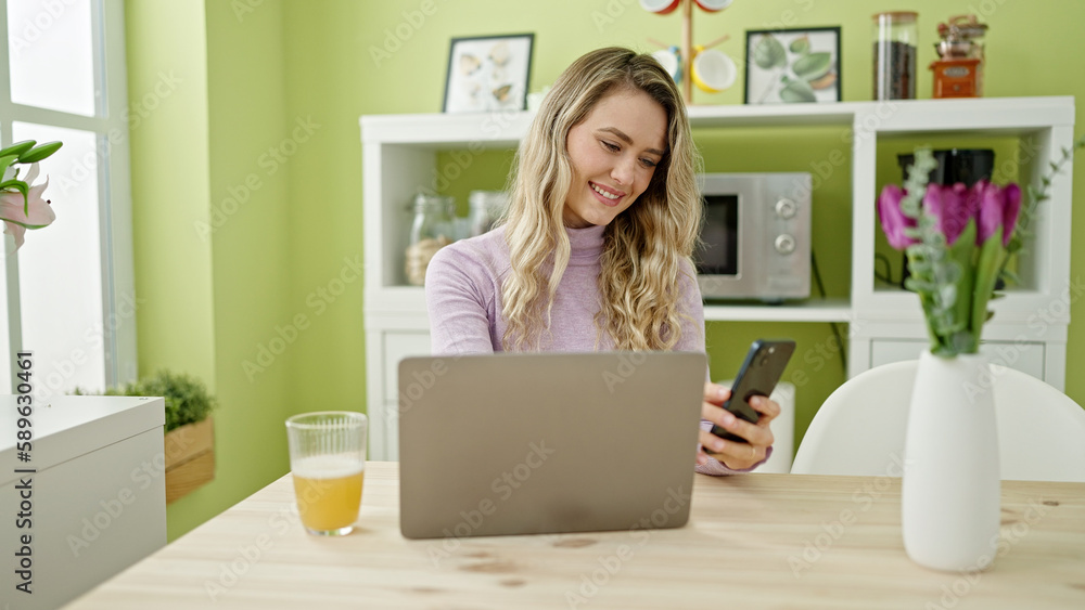 Sticker Young blonde woman using laptop and smartphone at dinning room