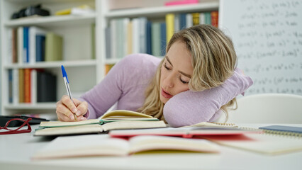 Young blonde woman student tired writing notes at classroom