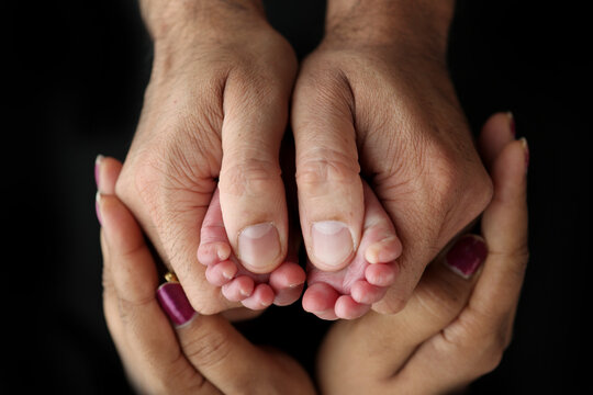 Feet of a newborn baby in the hands of parents. Happy Family oncept. Mum and Dad hug their baby's legs. Studio photography on black background of a child's toes, heels and feet. 