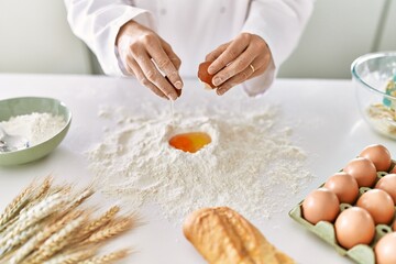 Young woman wearing cook uniform cracking egg on flour at kitchen