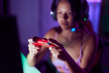 Young hispanic woman streamer playing video game at gaming room