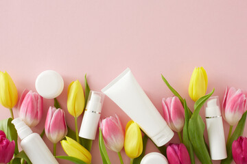 Natural skin care products concept. Top view photo of white cosmetic tubes without label spray bottles cream jars and pink yellow tulips on isolated pastel pink background with copy space