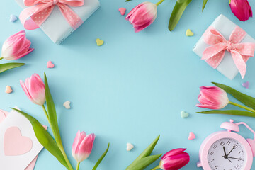 Obraz na płótnie Canvas Happy Mother's Day concept. Top view composition of gift boxes pink tulips flowers postcard alarm clock and small hearts baubles on isolated pastel blue background with empty space in the middle