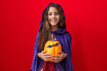 Little hispanic girl wearing witch halloween costume looking positive and happy standing and...