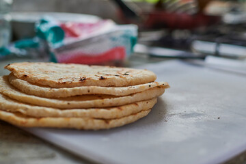 Round yellow arepas one on top of another pre-cooked on white plastic plate in small kitchen salt packet in blur background