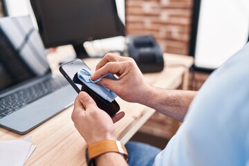 Young latin man ecommerce business worker cleaning screen smartphone at office