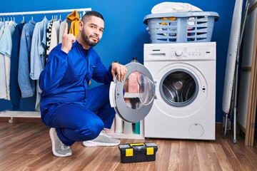 Hispanic repairman working on washing machine surprised with an idea or question pointing finger with happy face, number one