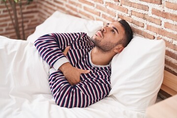 Young hispanic man stressed lying on bed at bedroom