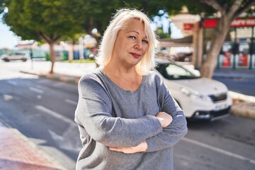 Middle age blonde woman standing relaxed with arms crossed gesture at street