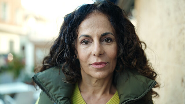 Middle age hispanic woman standing with relaxed expression at street