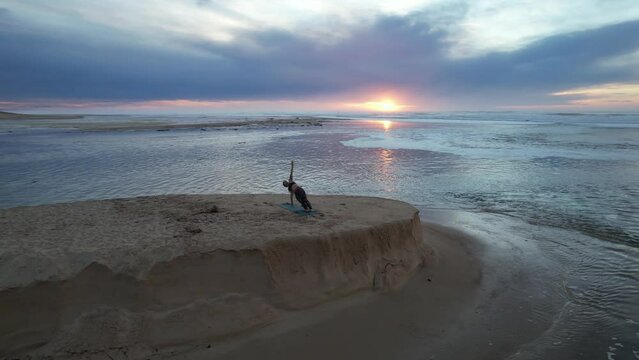 Impressive drone plan of the silhouette of a woman doing gracefully yoga at the beach near the natural reserve of the huchet current at sunset