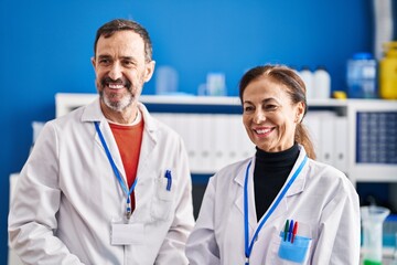 Middle age man and woman scientists smiling confident standing together at laboratory