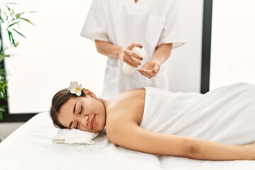Fototapeta na wymiar Young latin woman relaxed having back massage with moisturizer at beauty center