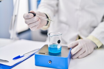 Young hispanic man wearing scientist uniform measuring liquid at laboratory