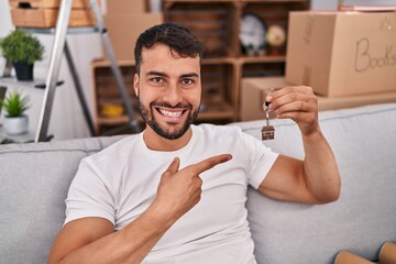 Handsome hispanic man holding keys of new home smiling happy pointing with hand and finger