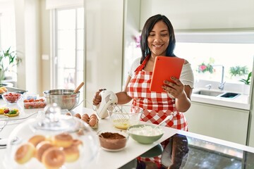 Hispanic brunette woman preparing cake looking at online recipe at the kitchen