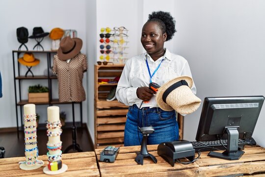 Young african american woman shopkeeper scanning hat using barcode reader at clothing store